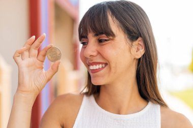 Açık havada elinde Bitcoin tutan genç bir kadın.