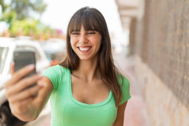 Açık havada cep telefonuyla selfie çeken genç bir kadın.