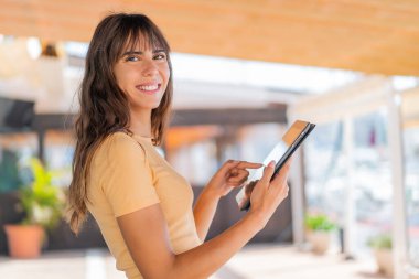 Dışarıdaki genç kadın tablet ekranına mutlu bir ifadeyle dokunuyor.