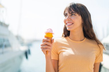 Dışarıda kornet dondurmalı genç bir kadın gülümserken yukarı bakıyor.