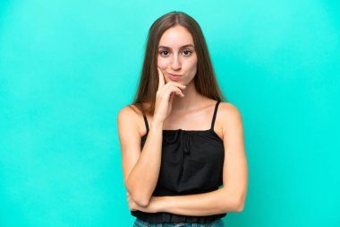 Kafkasyalı genç bir kadın mavi arka planda izole edilmiş ve düşünüyor