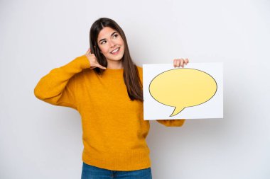 Beyaz arka planda izole edilmiş genç Brezilyalı bir kadın konuşma baloncuğu ikonlu bir levha tutuyor ve telefon hareketi yapıyor.