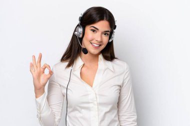 Beyaz arka planda izole edilmiş kulaklıkla çalışan beyaz pazarlamacı kadın parmaklarıyla tamam işareti gösteriyor.