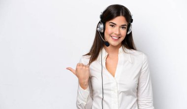 Beyaz arka planda izole edilmiş bir kulaklıkla çalışan beyaz pazarlamacı kadın bir ürünü sunmak için kenarı işaret ediyor.