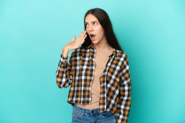 Mavi arka planda izole edilmiş genç bir Fransız kadın esniyor ve elleriyle ağzını kapatıyor.