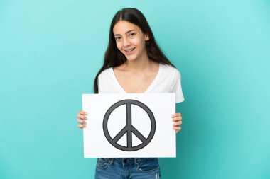 Mavi arka planda izole edilmiş genç bir Fransız kadın elinde mutlu bir ifadeyle barış sembolü olan bir pankart tutuyor.