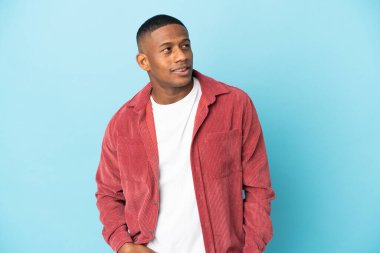 Genç latin adam mavi arka planda yalnız gülüyor.