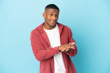 Genç latin adam mavi arka planda izole edilmiş alkışlıyor.