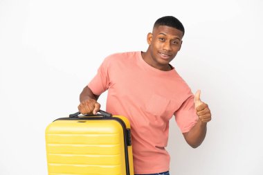Genç latin adam beyaz arka planda izole edilmiş seyahat valiziyle ve başparmağıyla