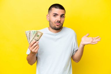 Kafkasyalı genç adam sarı arka planda izole edilmiş bir sürü para alıyor.