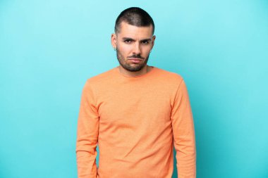 Hüzünlü bir ifadeyle mavi arka planda izole edilmiş genç beyaz bir adam.
