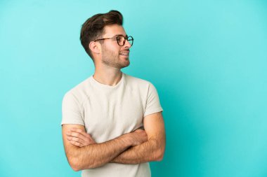 Genç beyaz yakışıklı adam mavi arka planda izole edilmiş mutlu ve gülümsüyor.