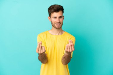 Beyaz tenli yakışıklı adam mavi arka planda izole edilmiş para hareketi yapıyor.