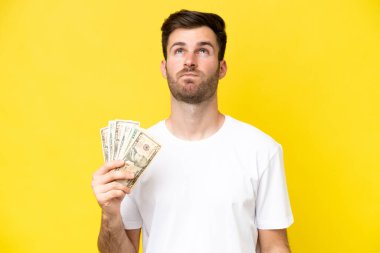 Kafkasyalı genç bir adam çok para alıyor. Sarı arka planda izole edilmiş ve araştırılıyor.