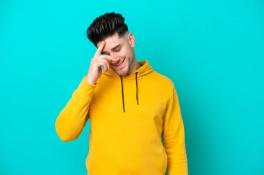 Kafkasyalı genç adam mavi arka planda tek başına gülüyor.