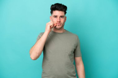 Mavi arka planda izole edilmiş genç beyaz bir adam sessizlik işareti gösteriyor.