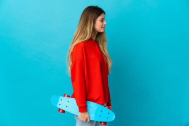 Genç sarışın kadın mavi arka planda tek başına paten kayıyor.