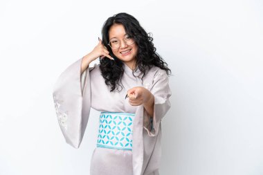 Kimono giyen genç Asyalı bir kadın beyaz arka planda izole edilmiş telefon hareketleri yapıyor ve ön tarafı işaret ediyor.