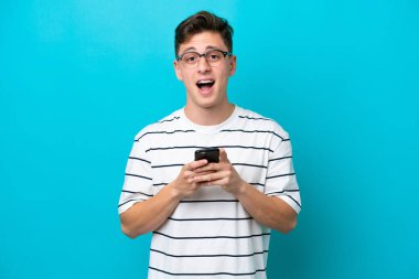 Mavi arka planda izole edilmiş yakışıklı Brezilyalı bir adam şaşırdı ve bir mesaj gönderiyor.