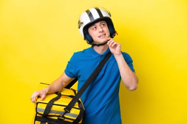 Termal sırt çantalı genç Brezilyalı adam sarı arka planda izole edilmiş bir şekilde yukarı bakarken bir fikir düşünüyor.