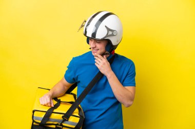 Sırt çantalı genç Brezilyalı adam sarı arka planda izole edilmiş, yana bakıyor ve gülümsüyor.