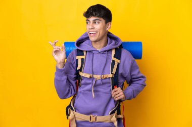 Young mountaineer man with a big backpack over isolated yellow background intending to realizes the solution while lifting a finger up