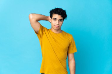 Genç Venezuelalı bir adam mavi arka planda bir hayal kırıklığı ifadesiyle izole edildi ve anlamadı.