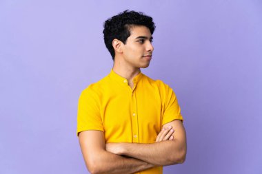Genç Venezuelalı adam, mor arka planda izole edilmiş, yan tarafa bakıyor.