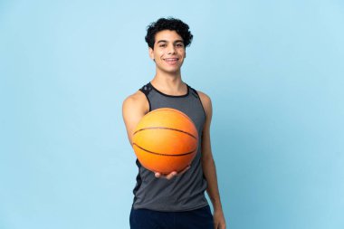 Genç Venezuelalı adam mavi arka planda izole edilmiş basketbol oynuyor.