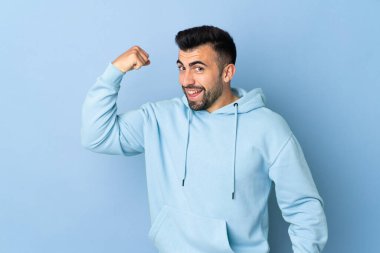İzole edilmiş mavi arka planda beyaz bir adam güçlü bir jest yapıyor.
