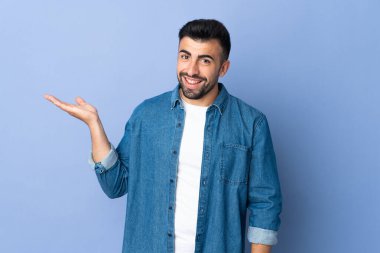 İzole edilmiş mavi arka plan üzerinde beyaz bir adam bir ilan vermek için avucunun içinde hayali bir mekan tutuyor.