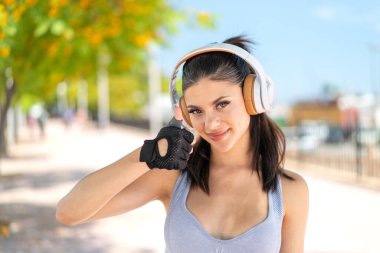 Açık havada müzik dinleyen ve başparmağını kaldıran genç ve güzel bir bayan.