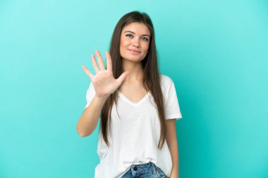 Mavi arka planda izole edilmiş genç beyaz kadın parmaklarıyla beşi sayıyor.
