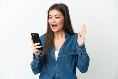 Young caucasian woman isolated on white background looking at the camera while using the mobile with surprised expression