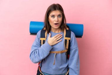 Pembe arka planda izole edilmiş büyük sırt çantalı genç dağcı kadın sağa bakarken şaşırdı ve şok oldu.