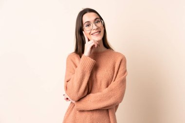 İzole edilmiş bej arka planı olan genç bir kadın yana bakıyor ve gülümsüyor.