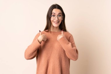 İzole edilmiş bej arka planı olan genç bir kadın. Şaşırtıcı yüz ifadesi var.