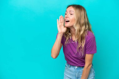 Mavi arka planda izole edilmiş genç Rus kadın ağzı sonuna kadar açık bağırıyor.