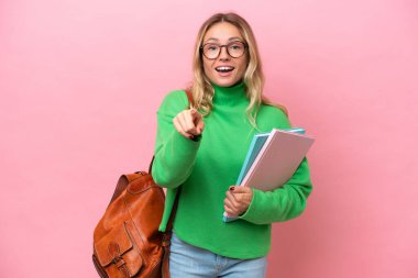 Pembe arka planda izole genç bayan şaşırmış ve ön tarafı işaret ediyor.