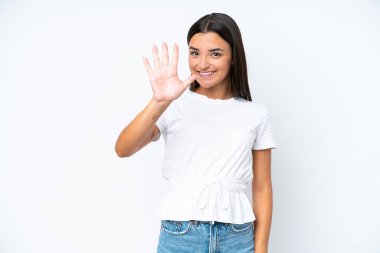 Beyaz arka planda izole edilmiş beyaz tenli genç kadın parmaklarıyla beşi sayıyor.