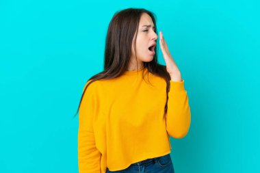 Genç Ukraynalı bir kadın mavi arka planda izole edilmiş esniyor ve geniş bir ağzı eliyle kapatıyor.