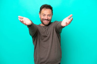 Middle age caucasian man isolated on blue background presenting and inviting to come with hand