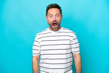 Orta yaşlı beyaz bir adam mavi arka planda izole edilmiş ve yüzünde sürpriz bir ifade var.