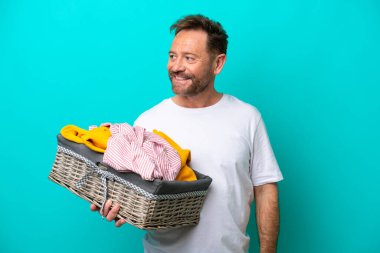 Mavi arka planda bir çamaşır sepetini tutan orta yaşlı kadın yana bakıyor ve gülümsüyor.