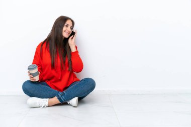 Genç Ukraynalı bir kadın beyaz arka planda izole bir şekilde oturuyor. Elinde kahve ve cep telefonu var.