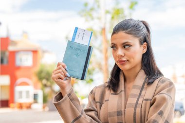 Dışarıda pasaport tutan genç ve güzel bir kadın. Üzgün bir ifadeyle.