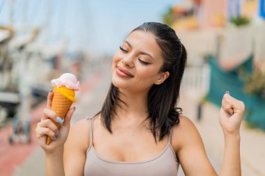 Açık havada kornet dondurmalı genç ve güzel bir kadın zaferi kutluyor.