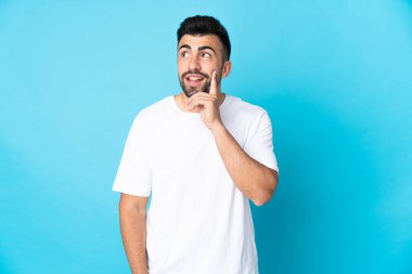 İzole edilmiş mavi arka plan üzerinde beyaz bir adam yukarı bakarken bir fikir düşünüyor.