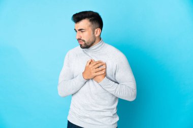İzole edilmiş mavi arka planı olan beyaz bir adamın kalbinde ağrı var.