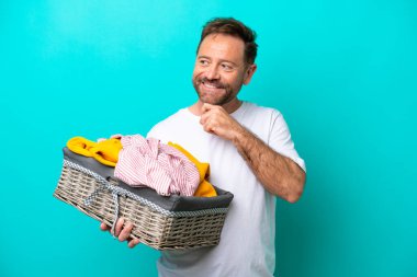 Mavi arka planda bir çamaşır sepetini tutan orta yaşlı kadın yana bakıyor ve gülümsüyor.